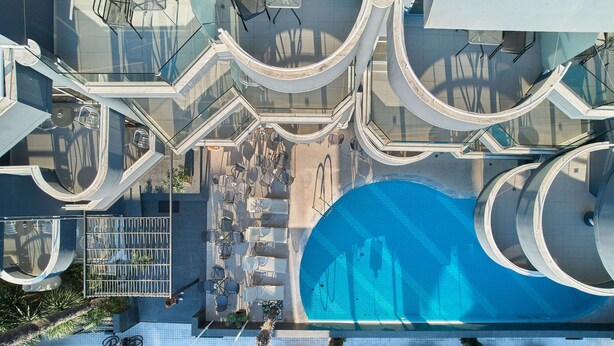 En moderne bygning med en central swimmingpool, udendørs siddepladser og gelænder af glas.