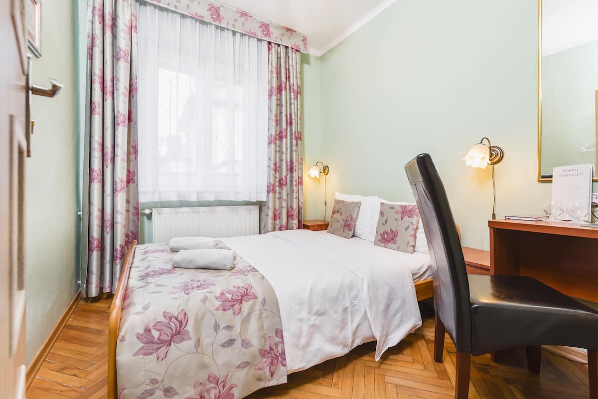 A hotel room with a bed, a desk, a chair, a nightstand, and a window with curtains.