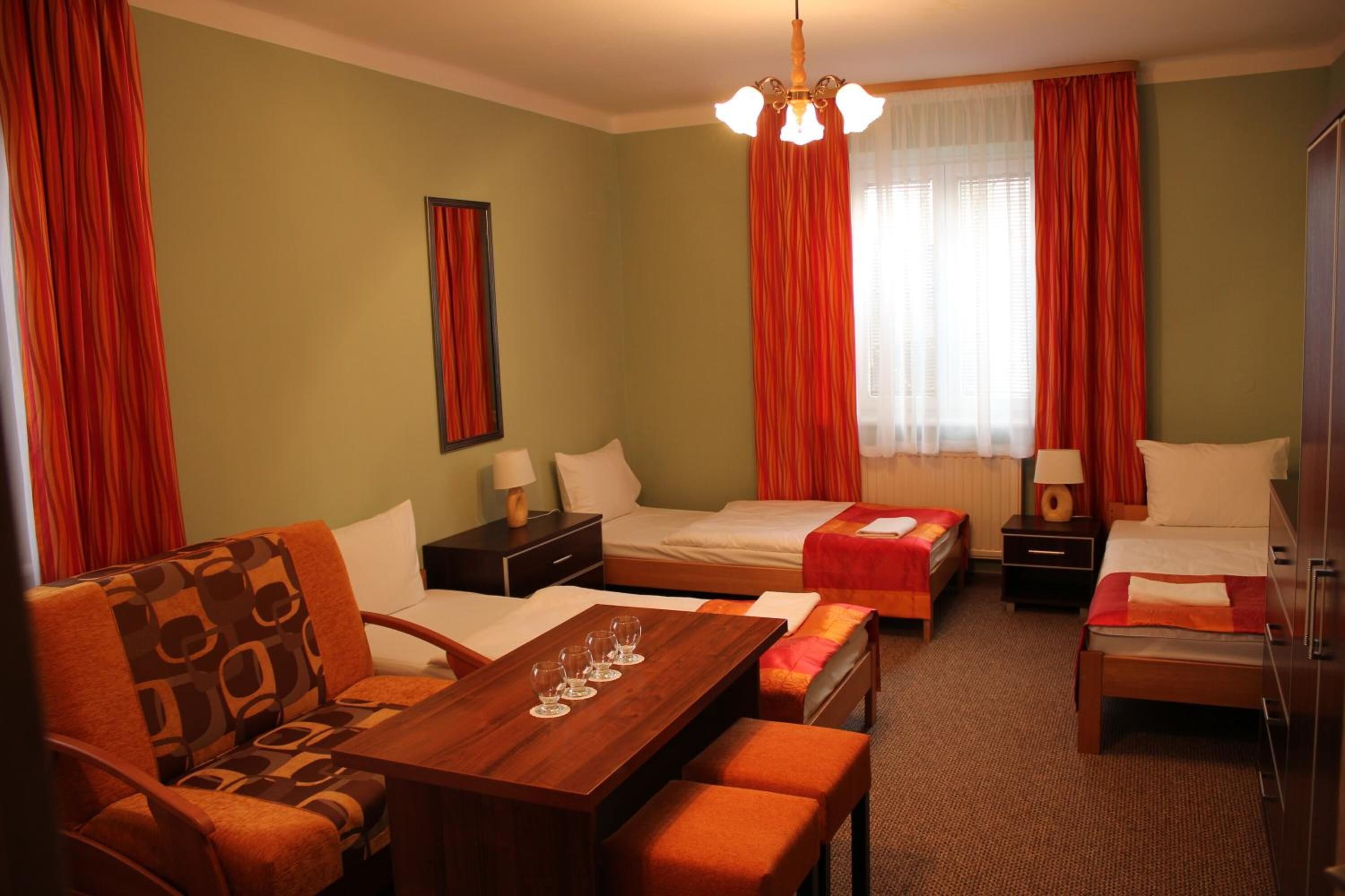 Habitación de hotel con dos camas individuales, un sofá, una mesa de comedor con vasos y una araña.