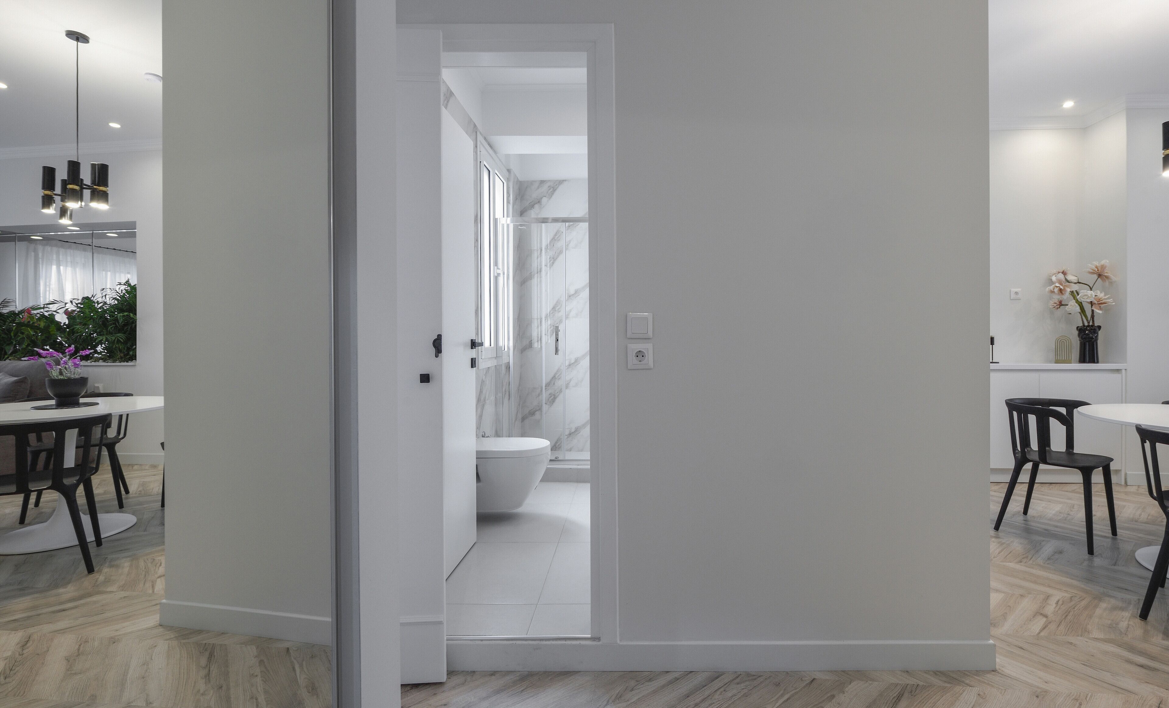 Une salle de bain moderne et minimaliste, avec des toilettes blanches, une douche en verre et un pare-baignoire en marbre.