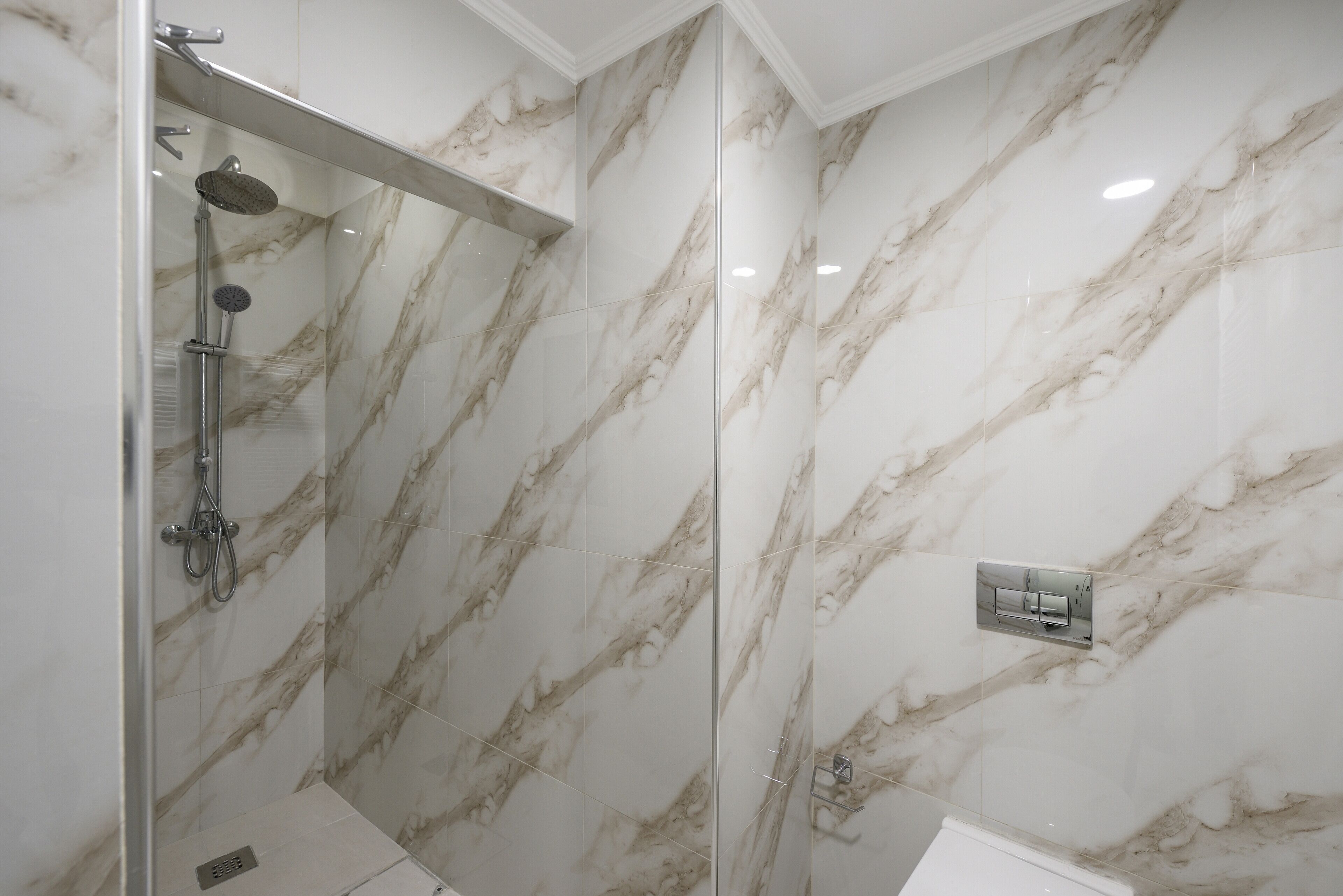 A modern bathroom with a glass-enclosed shower, marble walls, and a visible control panel.