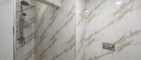 A modern bathroom with a glass-enclosed shower, marble walls, and a visible control panel.