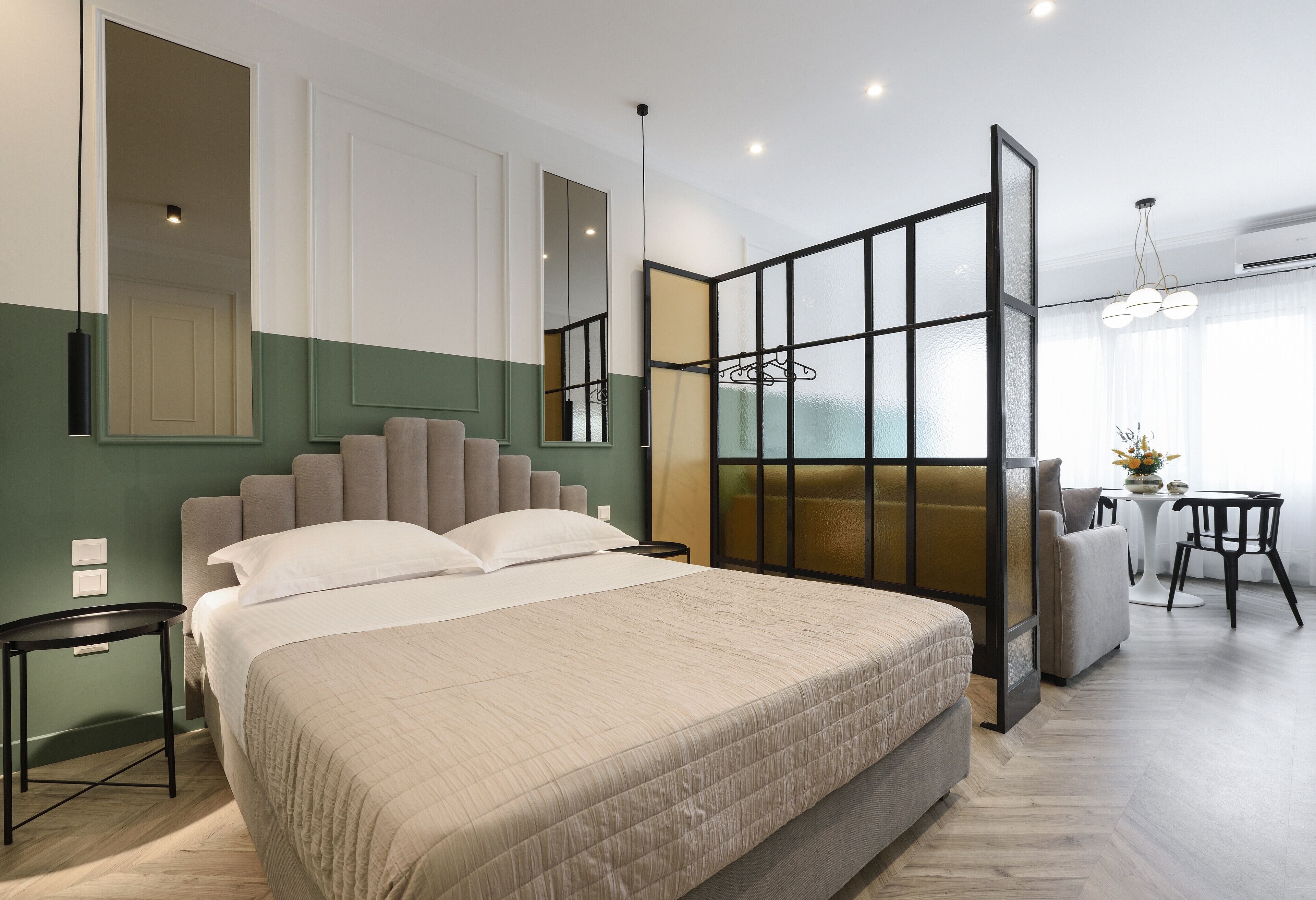 Habitación de hotel moderna con una cama grande, zona de estar con sofá y sillones, una mesita y un ventanal con vistas.
