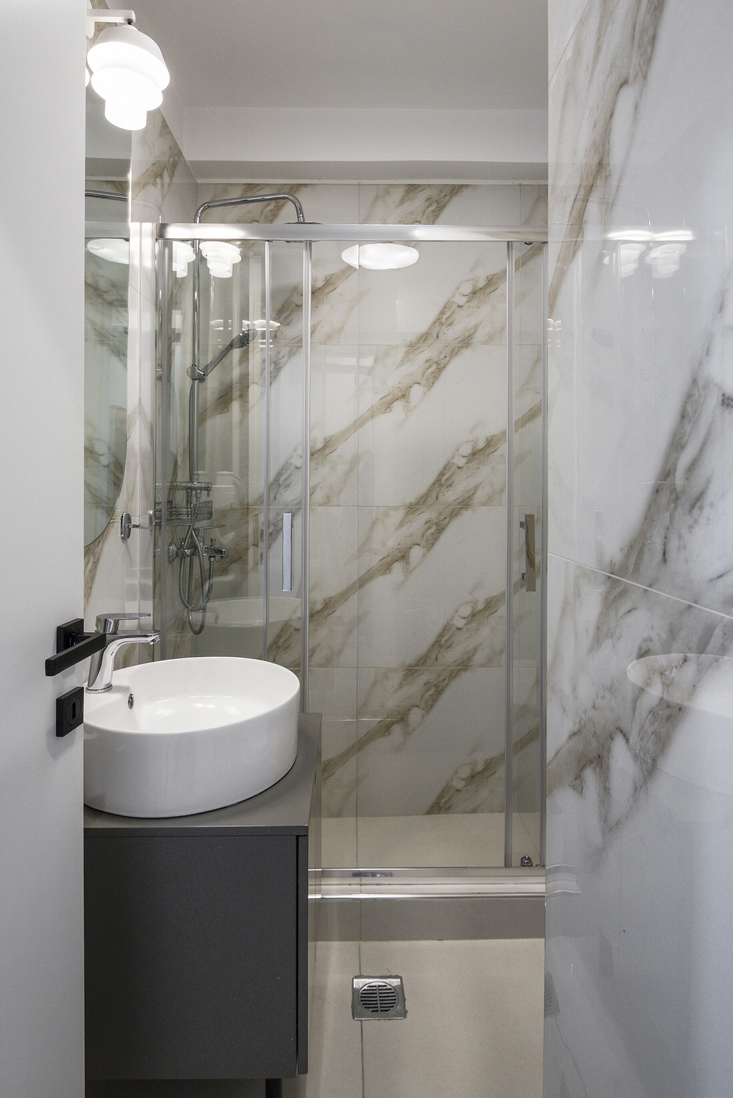 A modern bathroom with a glass-enclosed shower, a white sink, and marble walls.