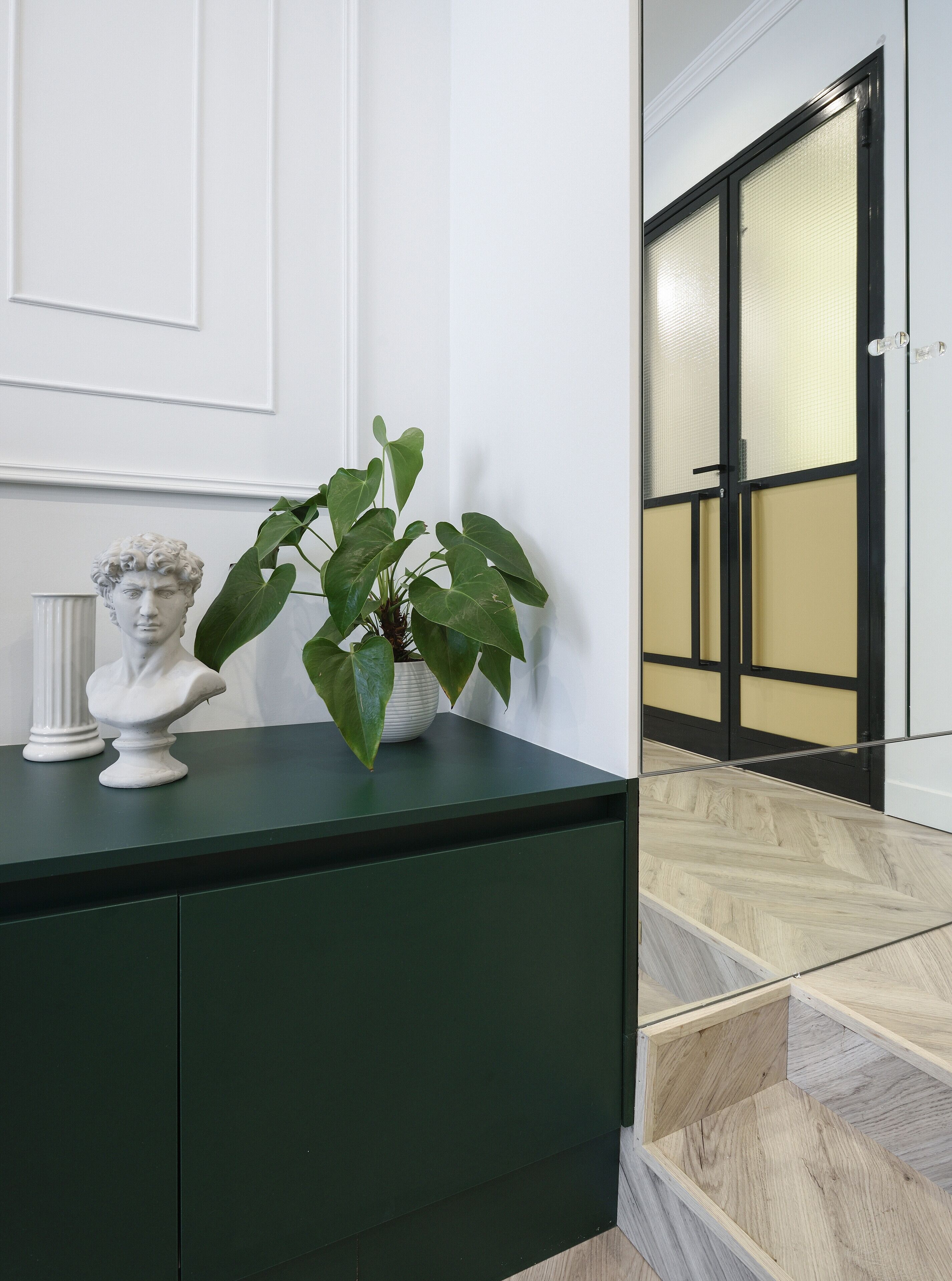 A marble bust on a dark green console table with a potted plant beside it.