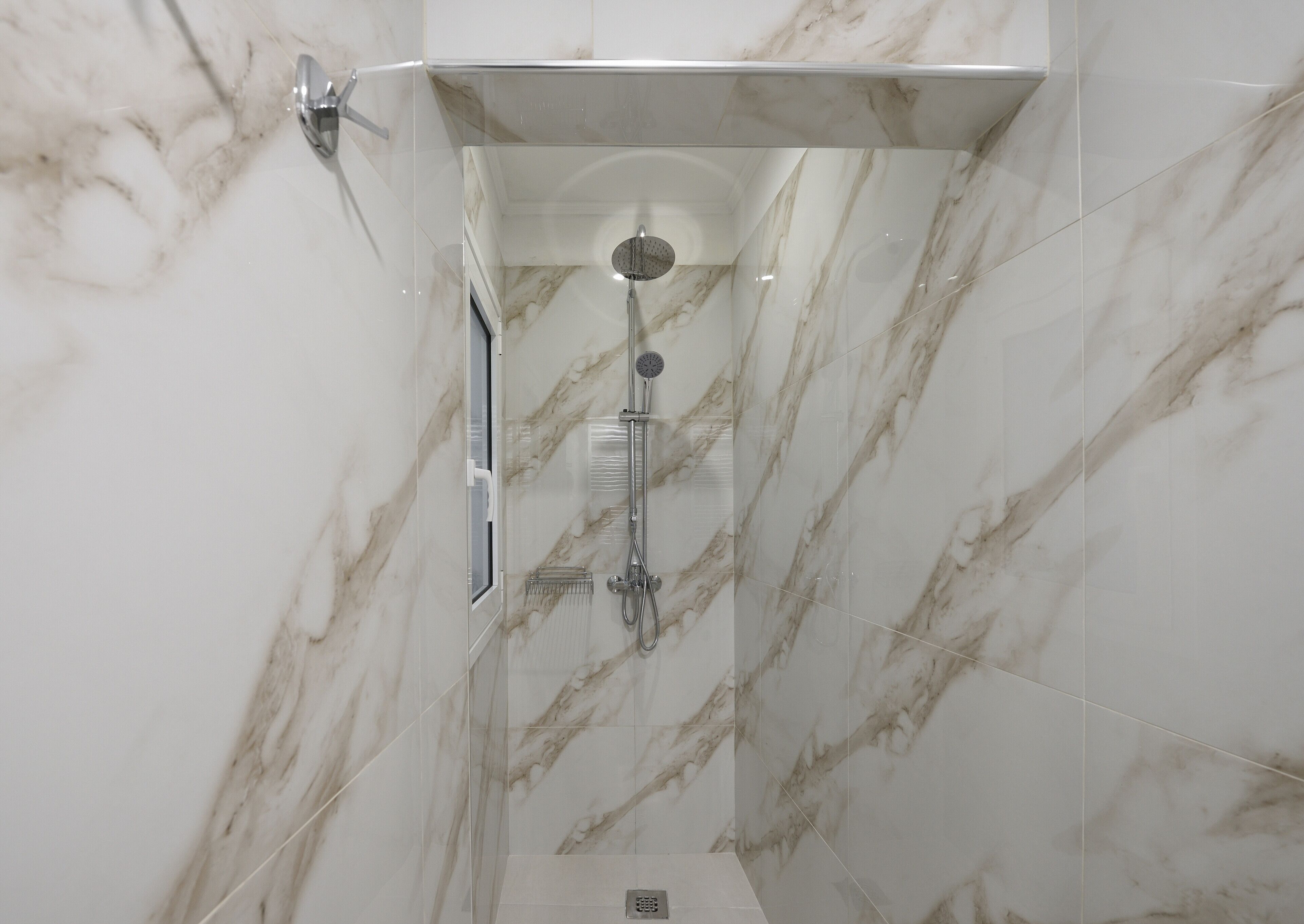 A modern shower with a glass enclosure, marble walls, and a handheld showerhead.