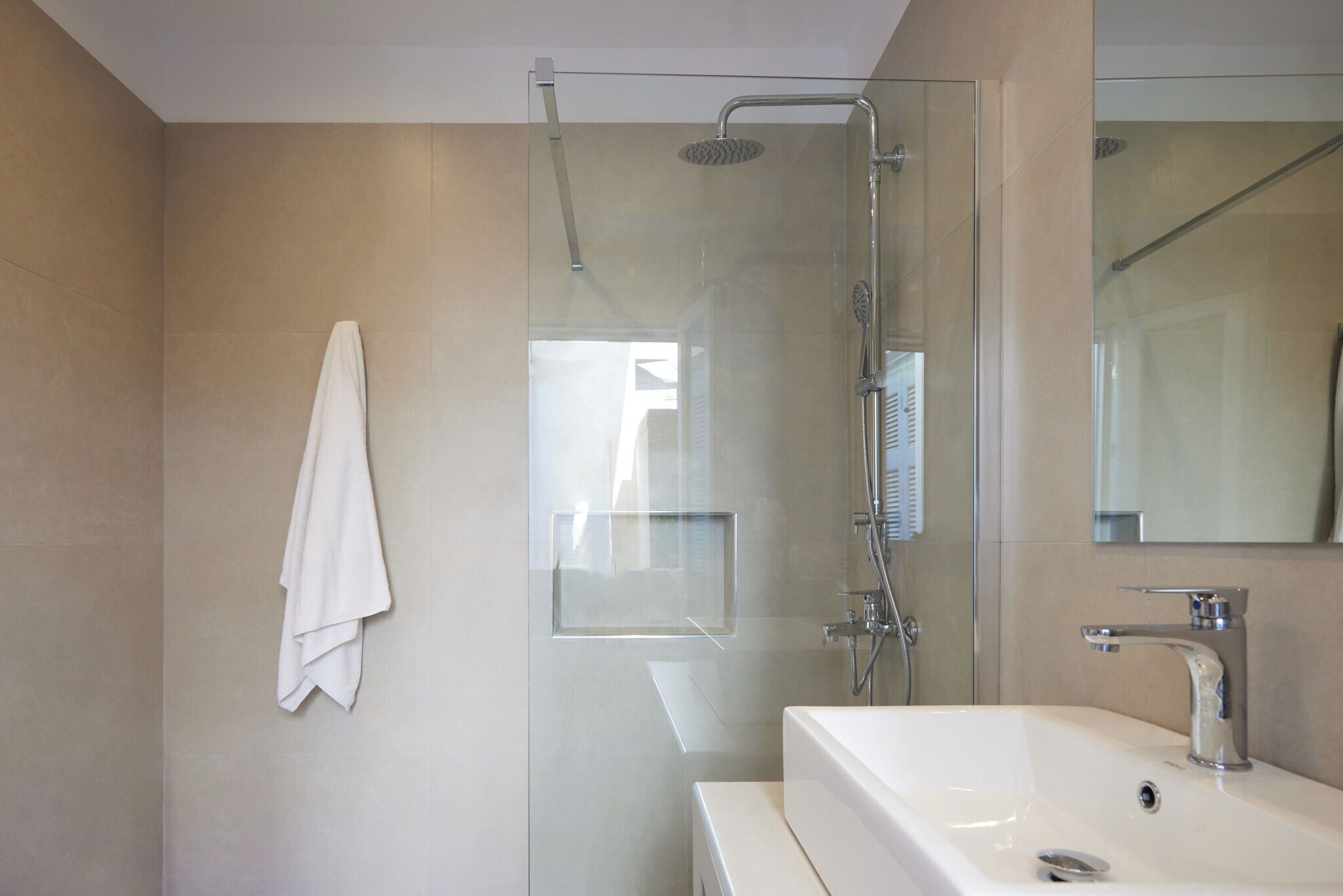 Une salle de bain moderne avec une douche à parois de verre, un lavabo blanc et une serviette accrochée au mur.