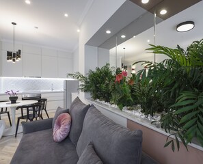 A modern living room with a grey sofa, a dining area with a white table and chairs, and a kitchen with white cabinets and a herringbone backsplash.