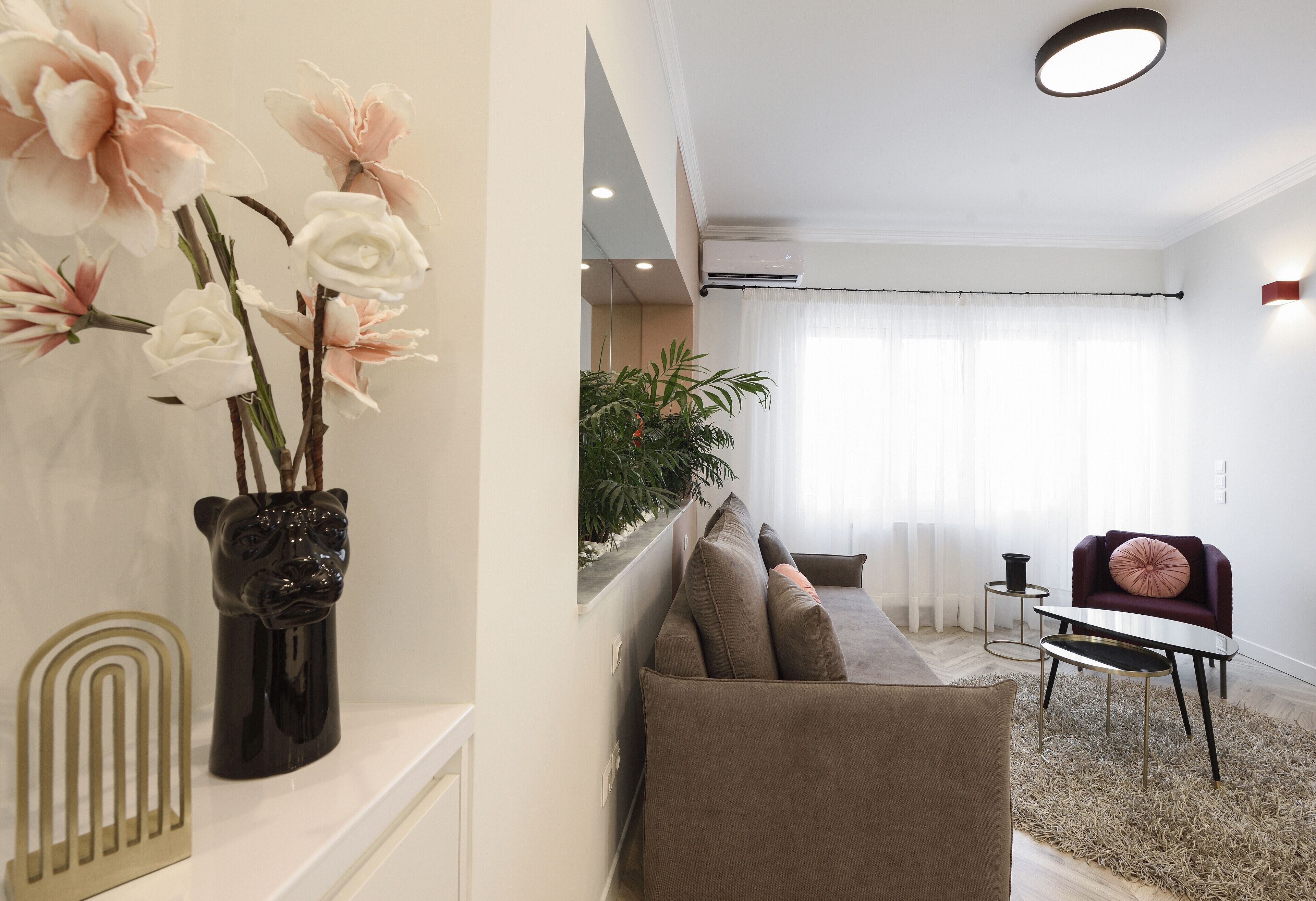 A modern living room with a sofa, a coffee table, and a chair. There is a vase with flowers on a shelf.