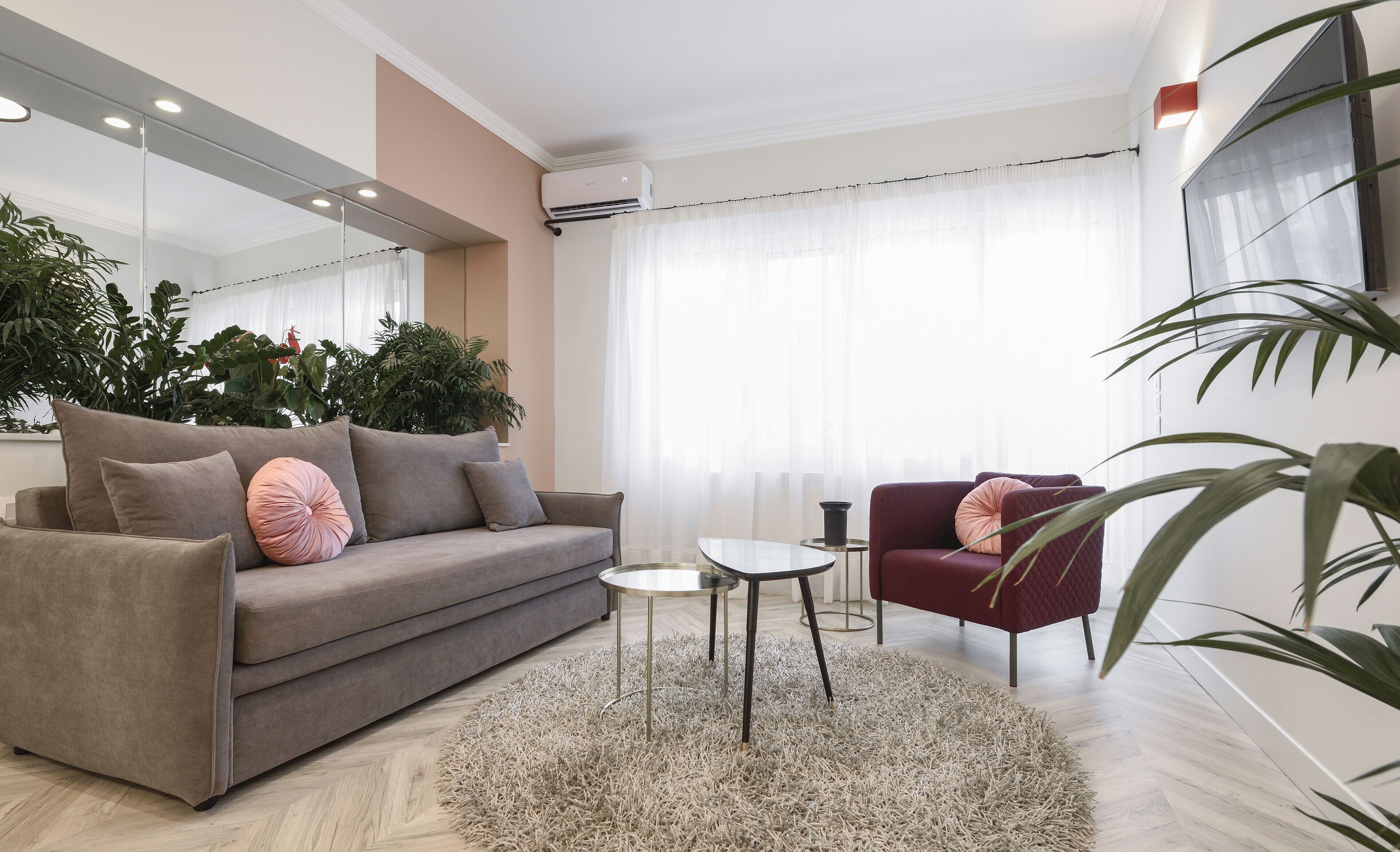 A modern living room with a sofa, a red armchair, a small table, and a large mirror.