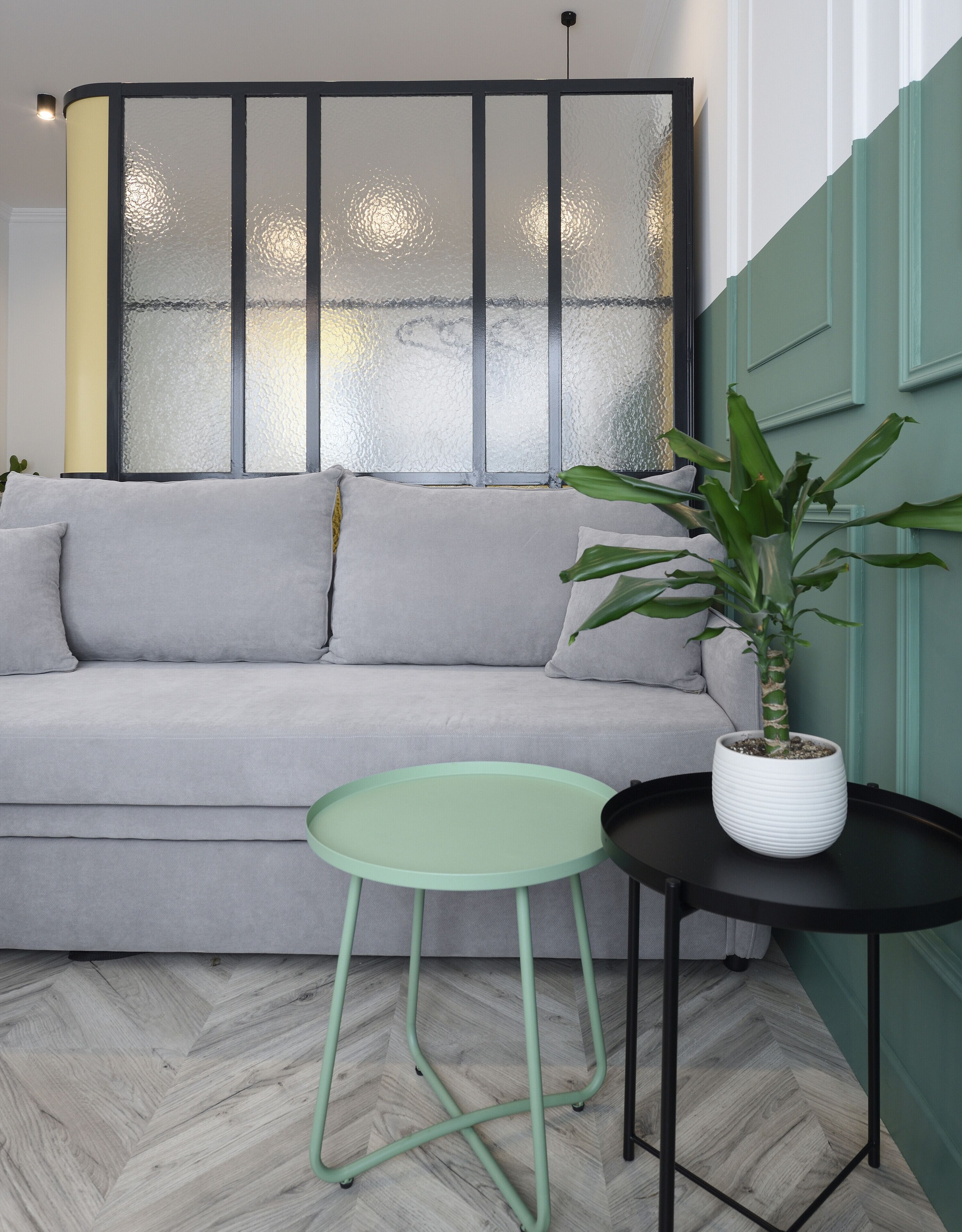 Ein modernes Wohnzimmer mit einer grauen Couch, einem kleinen runden Tisch und einer Topfpflanze.
