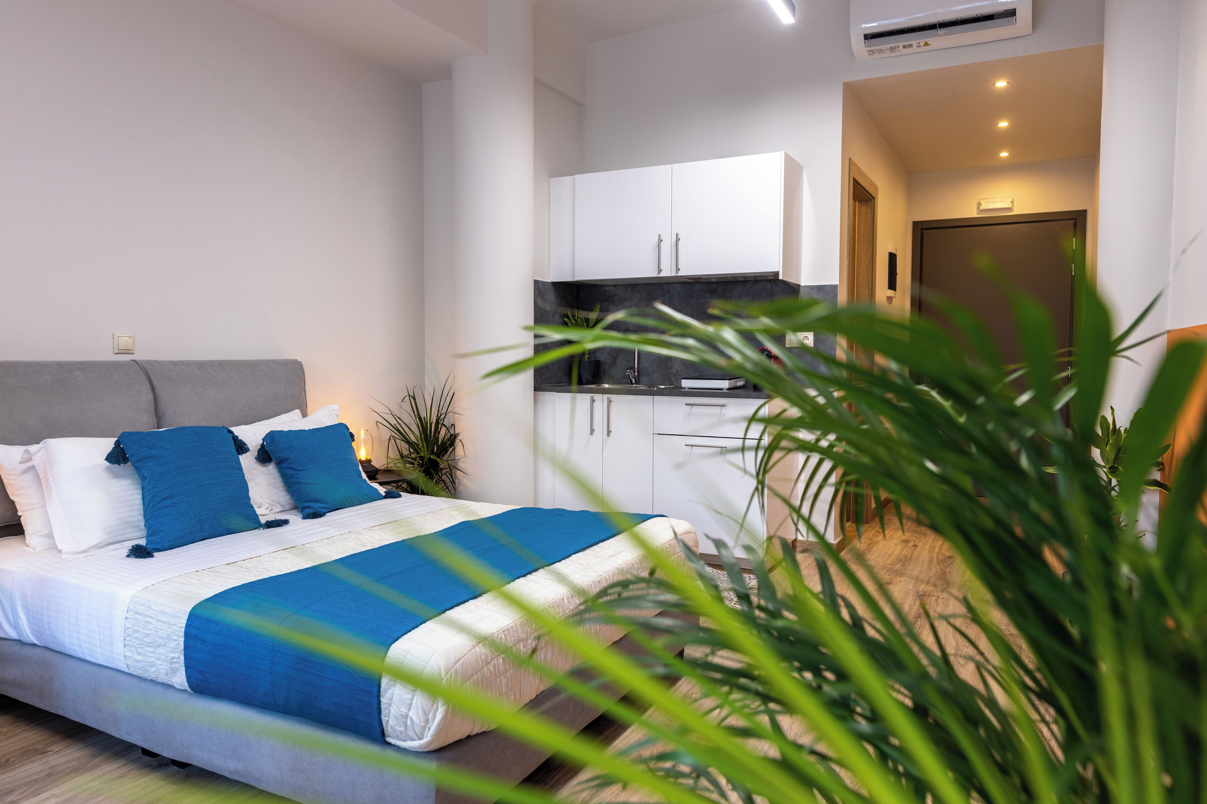 A modern bedroom with a bed, bedside tables, and a nightstand. There is a kitchen area with cabinets and a countertop.