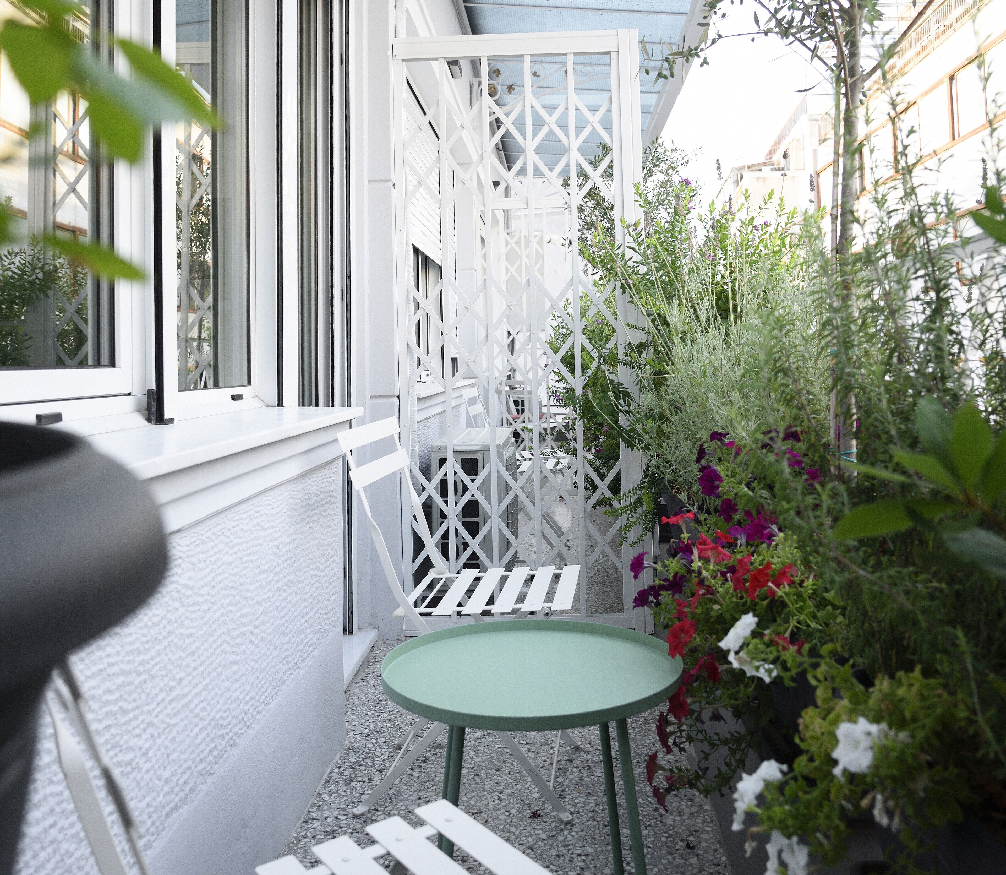 A small outdoor seating area with a table and chairs, surrounded by a white lattice fence and various plants.