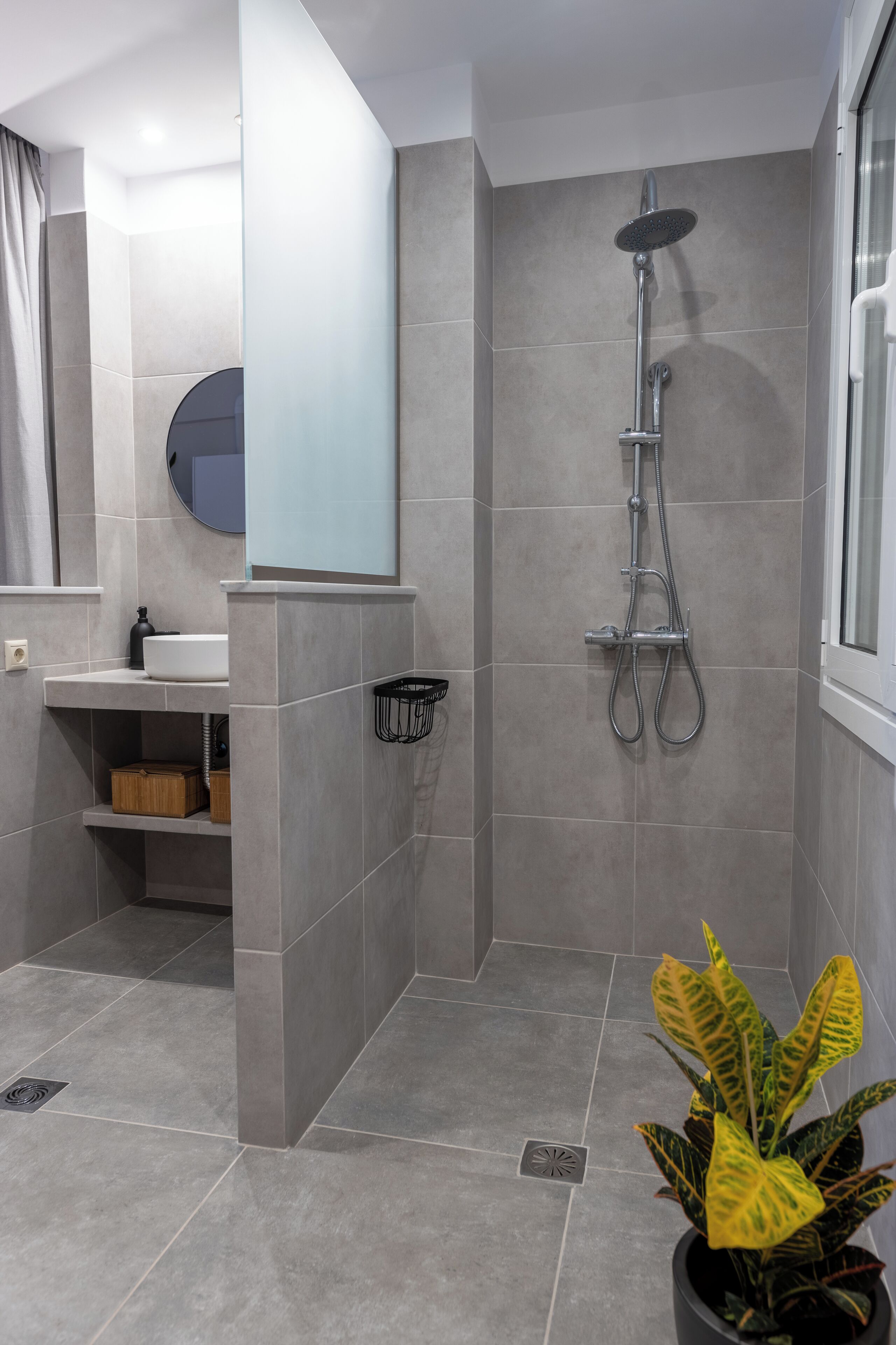 Un baño moderno con ducha, lavabo, espejo y una planta en maceta.