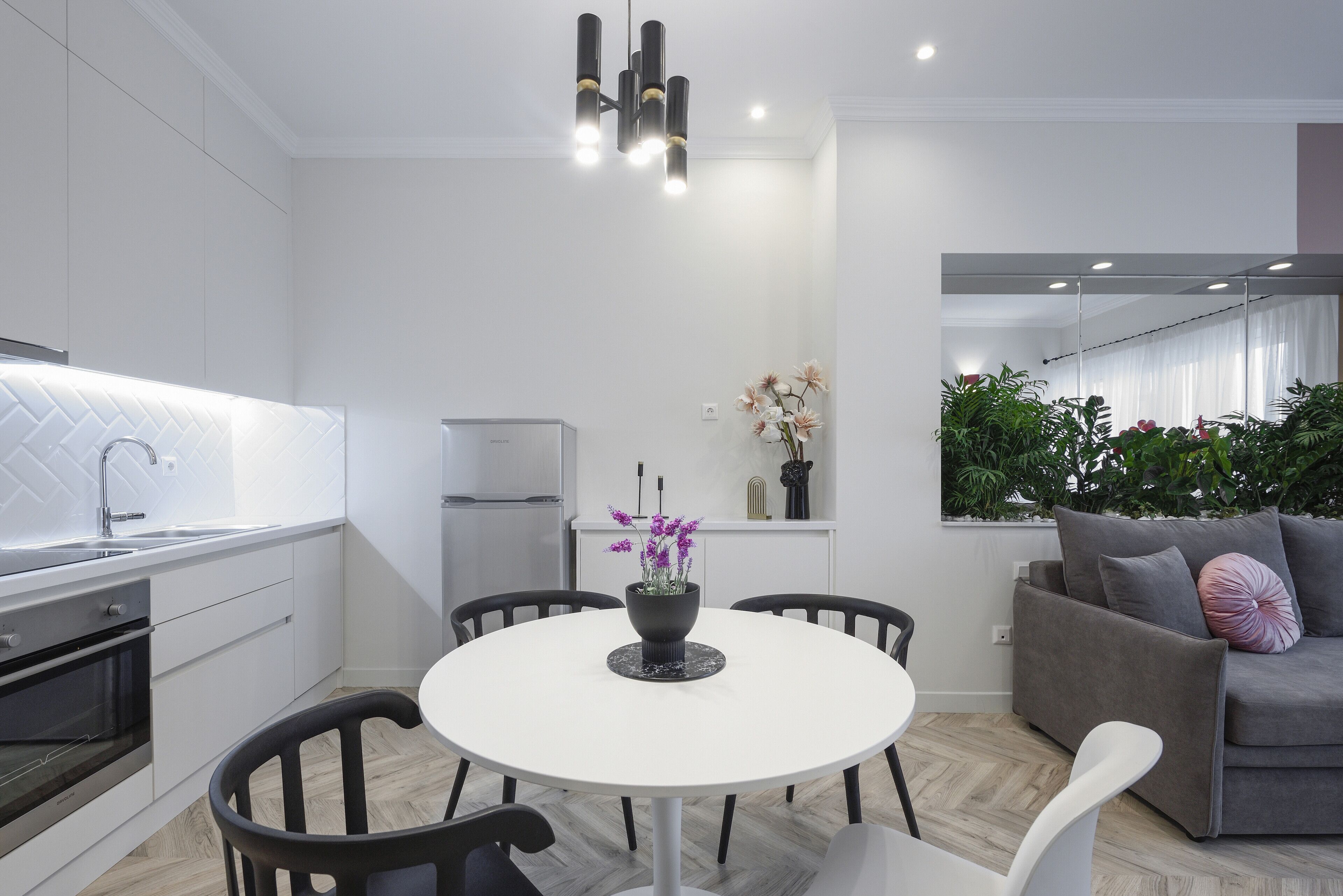 A modern kitchen with white cabinetry, a central island with a vase of flowers, and a dining area with a white table and black chairs.