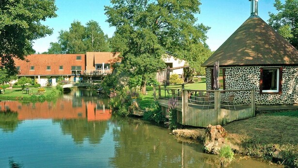 A riverside view with a small stone building and a wooden bridge. - Holiday Farm in Pfaffenhofen with Indoor Pool (Kindwiller)
