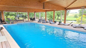 A wooden deck with a pool, lounge chairs, and a view of the countryside. - Holiday Farm in Pfaffenhofen with Indoor Pool (Kindwiller)