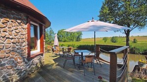 A stone building with a wooden deck, outdoor seating, and a view of a green landscape. - Holiday Farm in Pfaffenhofen with Indoor Pool (Kindwiller)