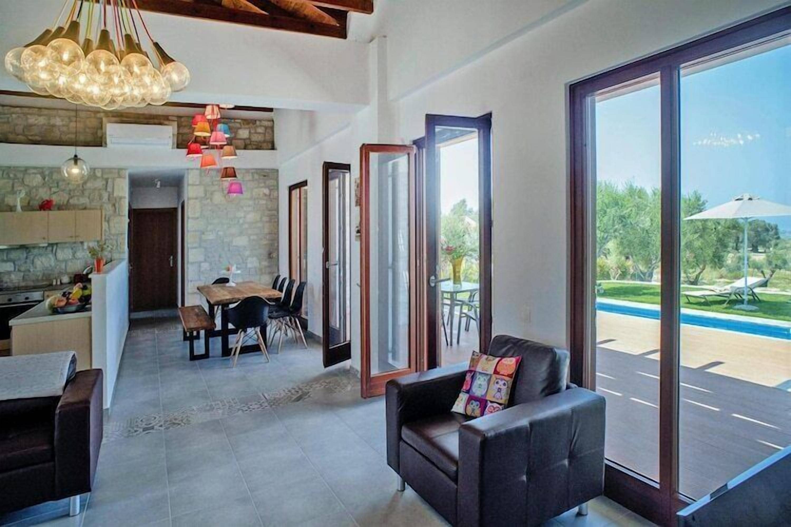 Ampla sala de estar com mesa de jantar, sofá e janelas grandes que dão para uma piscina.