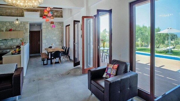 A spacious living area with a dining table, a sofa, and large windows offering a view of a swimming pool.