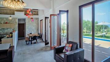 Ampla sala de estar com mesa de jantar, sofá e janelas grandes que dão para uma piscina.