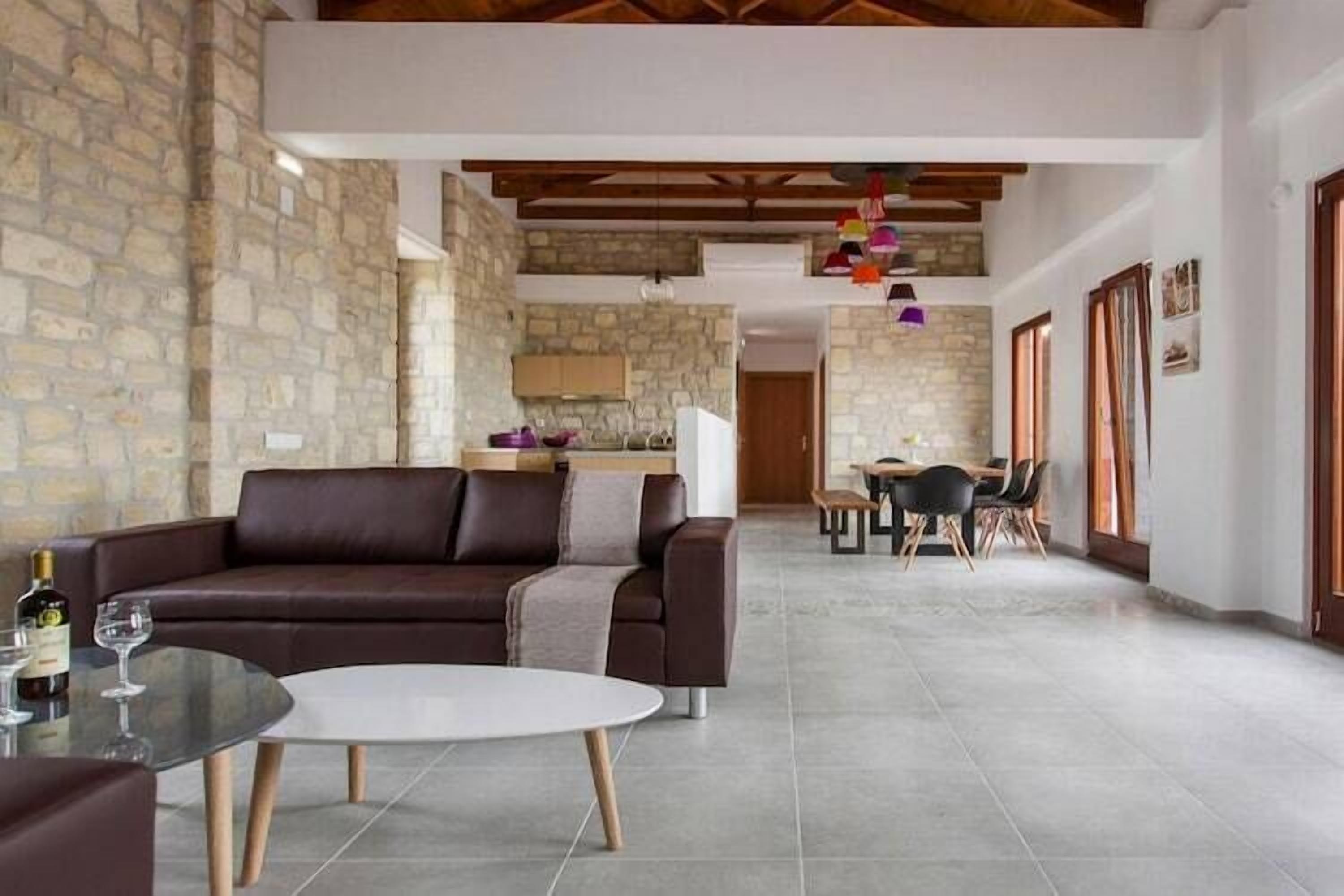 Uma sala de estar moderna com um sofá de couro marrom, uma mesa de centro de vidro e uma área de jantar com mesa e cadeiras de madeira.
