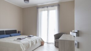 Un dormitorio con cama, una silla, un escritorio y una ventana con cortinas.