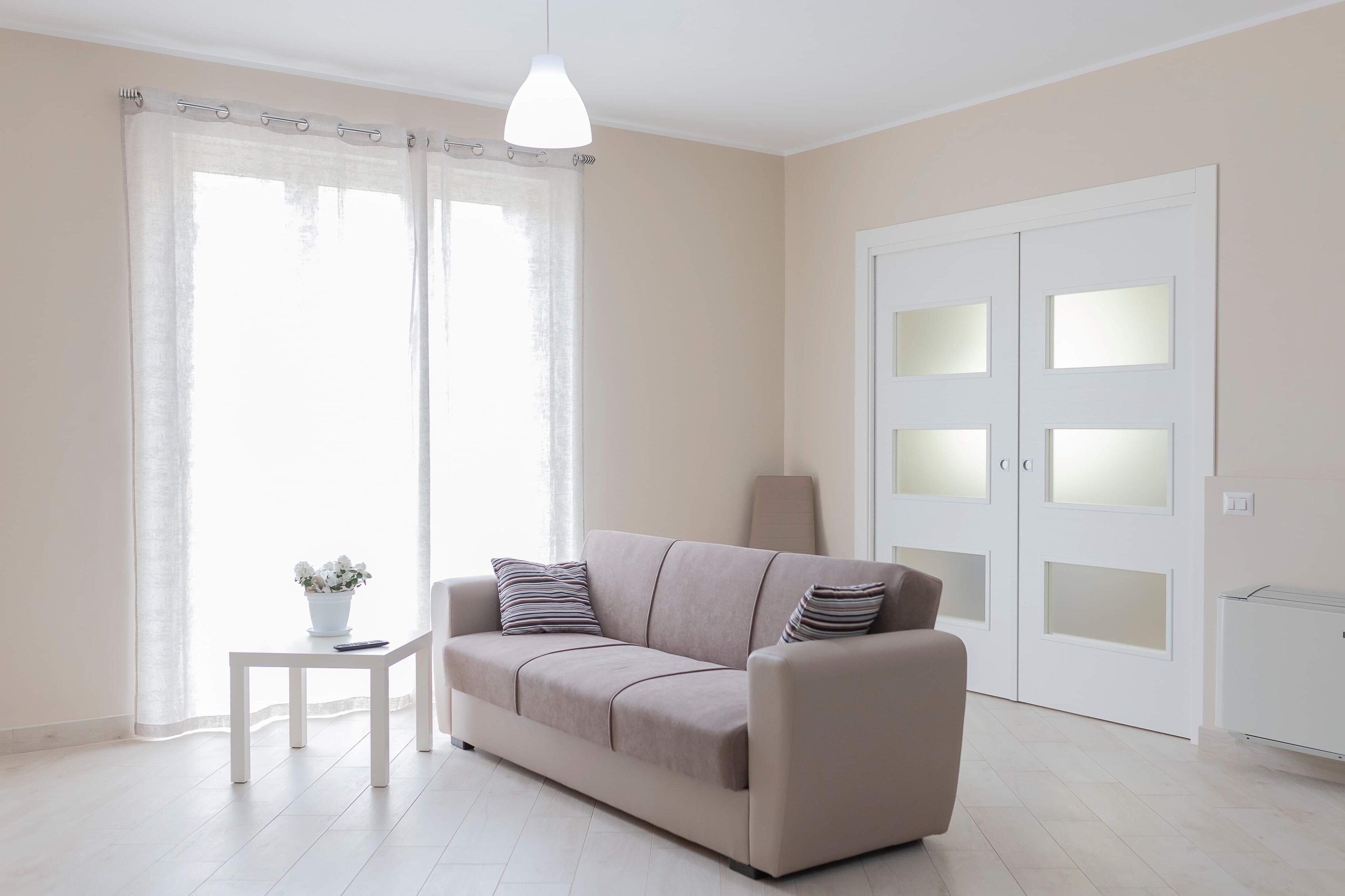 A modern living room with a beige sofa, a small white table with a plant, and a white radiator.