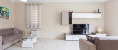 Una sala de estar moderna con un sofá, una mesa de centro de vidrio, un televisor de pantalla plana y una estantería minimalista.