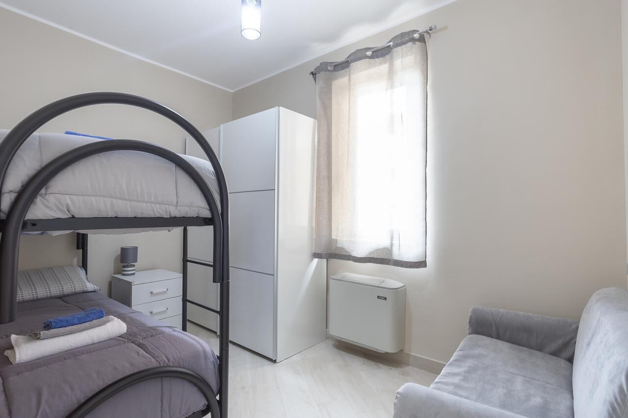 Een kleine slaapkamer met stapelbedden, een kledingkast, een radiator en een slaapbank.