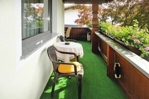 A small balcony with a table and chairs, a wooden railing, and a view of a garden with various plants.