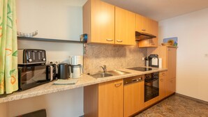 A compact kitchen with wooden cabinets, a microwave, toaster, coffee maker, and a sink. - Apartment in Fügen near Spieljochbahn (Fügen)