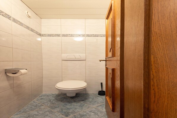 Un baño pequeño con azulejos, un inodoro, un dispensador de toallas de papel y un desatascador.