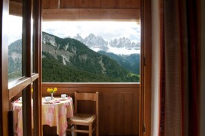 A wooden cabin with a balcony, a table with a tablecloth, a chair, and a vase with flowers.