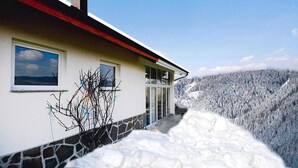 A house with a stone foundation, a red roof, and a view of a snow-covered mountain.