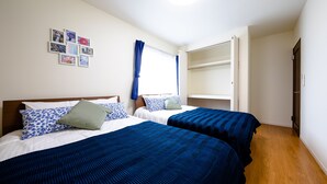 Quarto com duas camas, uma janela com cortinas azuis e uma parede com quadros.