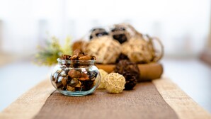 Um pote de vidro cheio de frutos secos e dois doces esféricos sobre uma superfície de madeira.
