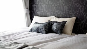 A neatly made bed with white and patterned pillows, a dark patterned headboard, and a sheer curtain partially drawn to the side. - Erable Mt.Fuji Zen (Fujikawaguchiko)