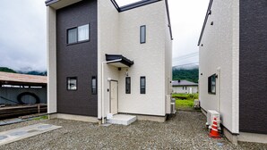 A modern two-story building with a combination of dark and light brick facades, a small entrance with steps, and a gravel driveway. - Erable Mt.Fuji Zen (Fujikawaguchiko)