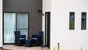 A modern building with a brick facade and a white exterior. There is a covered outdoor seating area with two chairs and a table. - Erable Mt.Fuji Zen (Fujikawaguchiko)