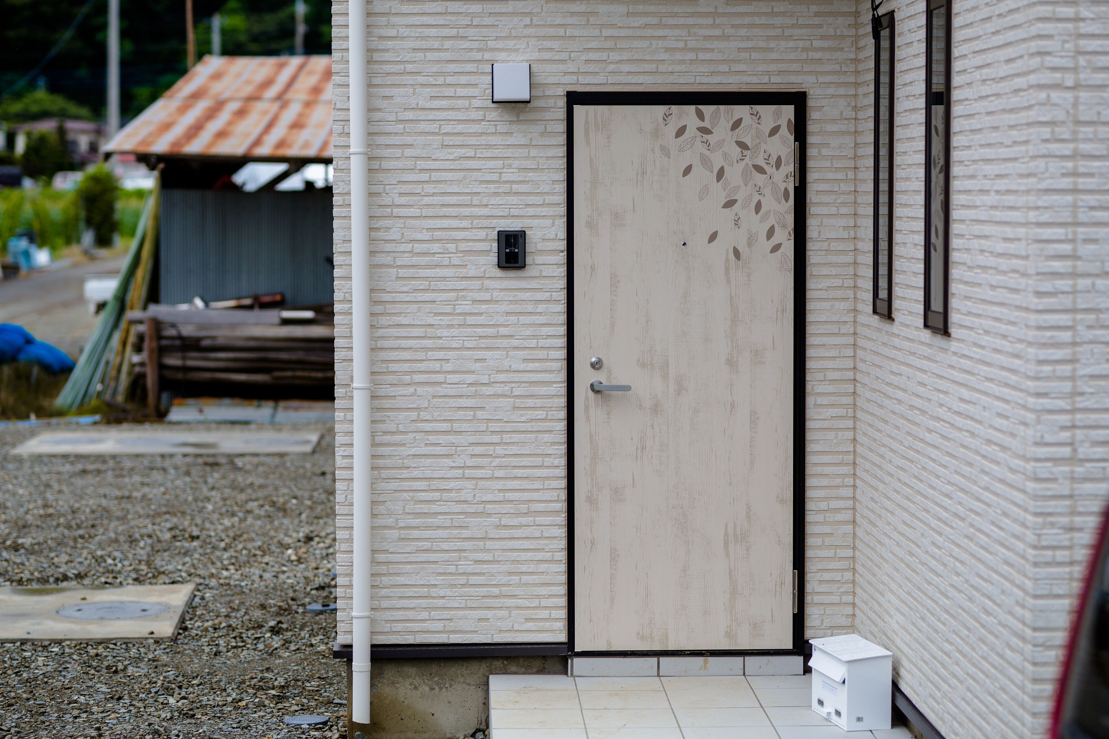A building with a wooden door, a small window, and a metal box on the wall.