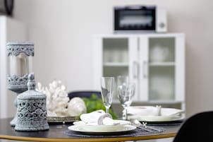 A dining table set with white plates, silverware, and clear glasses, with decorative items and a cabinet in the background.