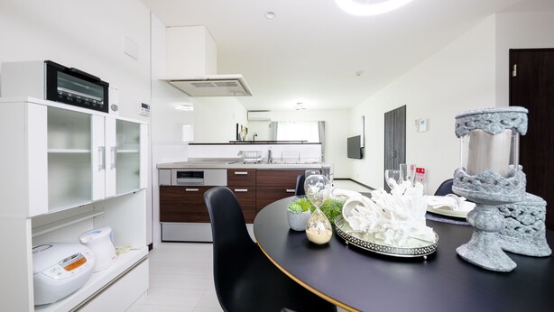 Une cuisine moderne avec des meubles blancs, un plan de travail noir et un coin repas comprenant une chaise noire et une table agrémentée d’objets décoratifs.