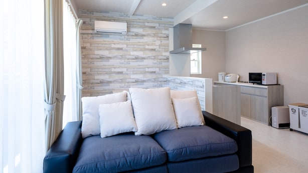 Una sala de estar moderna con un sofá modular, una zona de cocina con electrodomésticos y una pared con diseño de piedra.