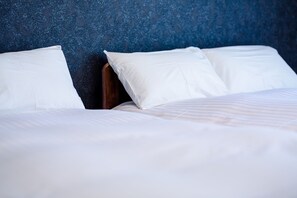 A neatly made bed with white linens and pillows, set against a dark blue textured wall. - Mt. View A (Fujikawaguchiko)