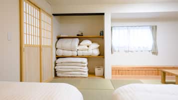 A traditional Japanese room with tatami flooring, a futon bed, a wooden shelf with pillows, and a sliding door.