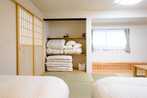Um quarto japonês tradicional com tatames, futon, prateleira de madeira com almofadas e porta deslizante.