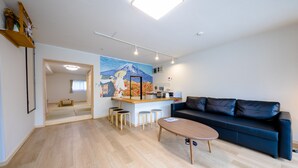 Un salon moderne avec un canapé, une table basse et un petit coin cuisine équipé de tabourets.