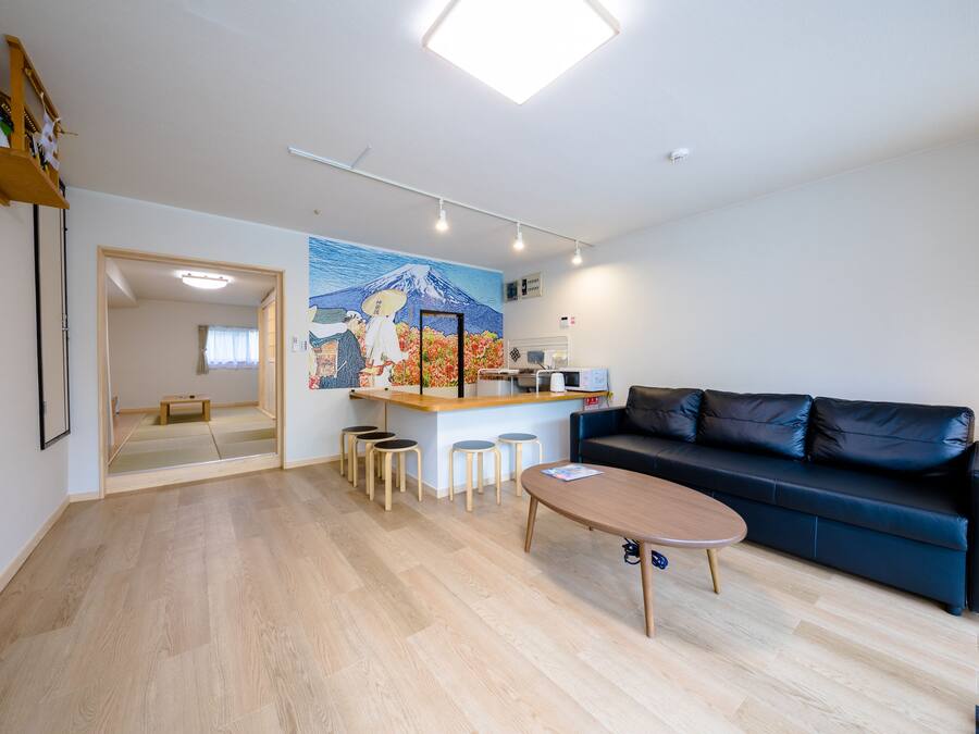 A modern living room with a sofa, a coffee table, and a small kitchen area with stools.