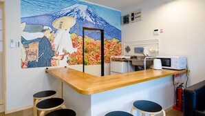 Une pièce avec un comptoir en bois, deux tabourets, un four à micro-ondes et une fresque murale représentant le mont Fuji.